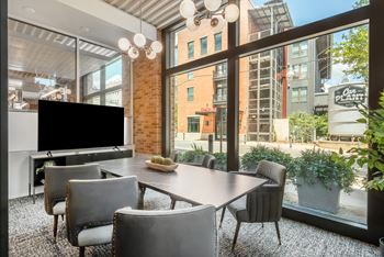 A dining room with a large window and a table with chairs and a television